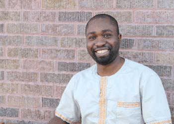 Henry smiling and sitting outside Amore Coffee against a brick wall